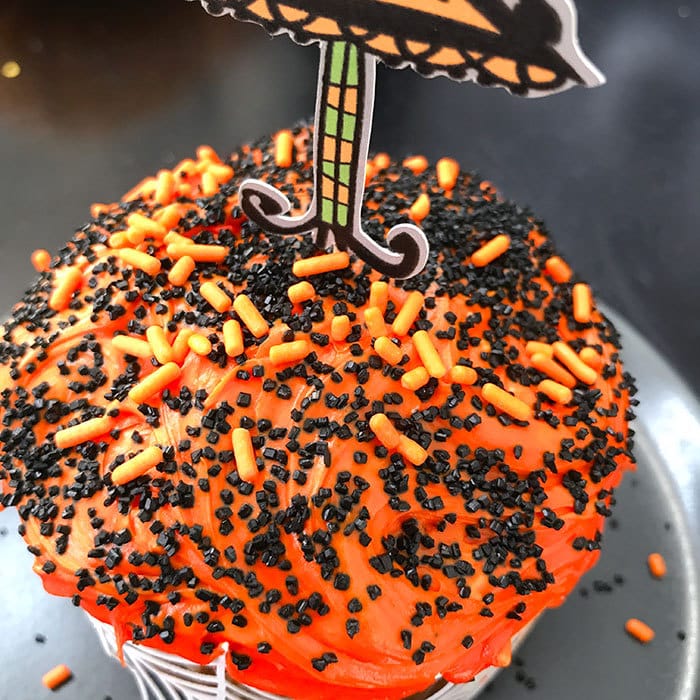 Decorate a cupcake with orange frosting and sprinkles and top with witch decoration.